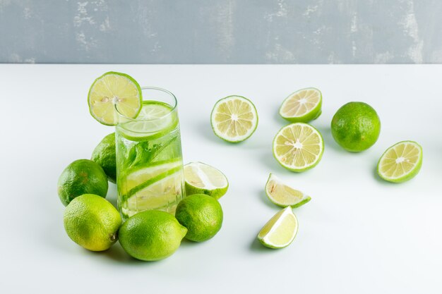Limonata con limoni, erbe aromatiche in un bicchiere su bianco e gesso, veduta dall'alto.