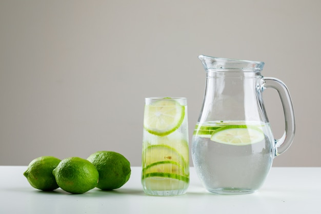 Limonata con limoni in vetro e brocca su bianco e grigio,