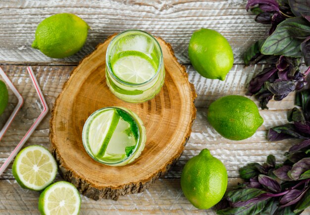 Limonata ghiacciata con limoni, basilico, cannucce in bicchieri su legno e tagliere, vista dall'alto.