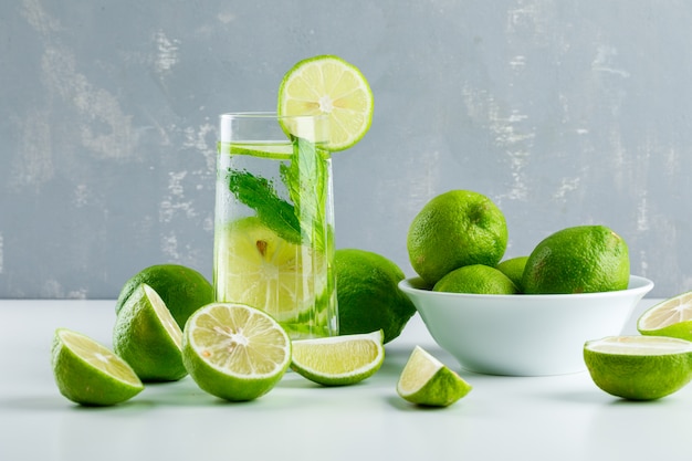 Limonata in un bicchiere con limoni, erbe vista laterale su bianco e gesso