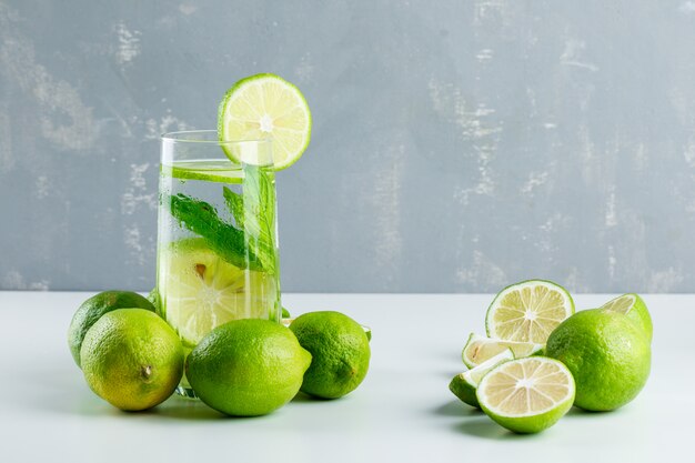 Limonata in un bicchiere con limoni, erbe vista laterale su bianco e gesso