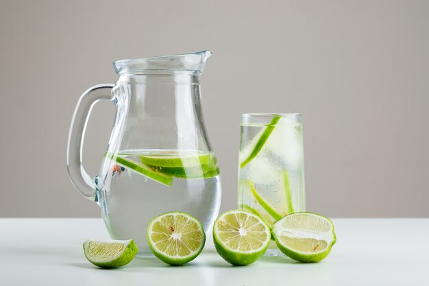 Limonata in vetro e brocca con vista laterale di limoni su bianco e grigio