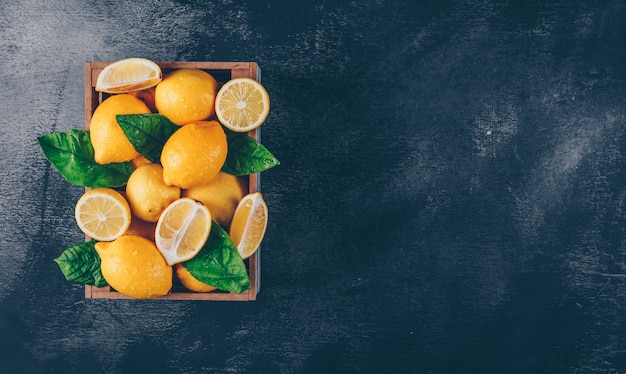 Limoni con le fette e le foglie in una scatola di legno su fondo strutturato nero, vista superiore. copia spazio per il testo