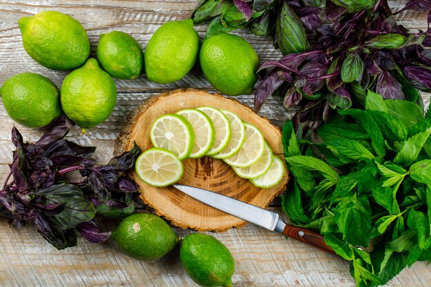 Limoni con mazzi di basilico, coltello sul tagliere di legno e, piatto disteso.