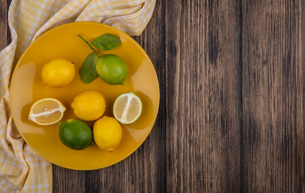 Limoni dello spazio della copia di vista superiore con limette sulla zolla gialla con l'asciugamano a scacchi giallo su fondo di legno