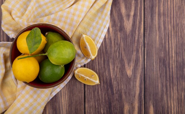 Limoni di spazio copia vista dall'alto con limette in una ciotola su un asciugamano a scacchi giallo su uno sfondo di legno