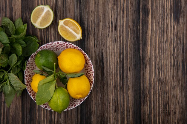 Limoni di spazio copia vista dall'alto con limette su un piatto con spicchi e menta su fondo in legno