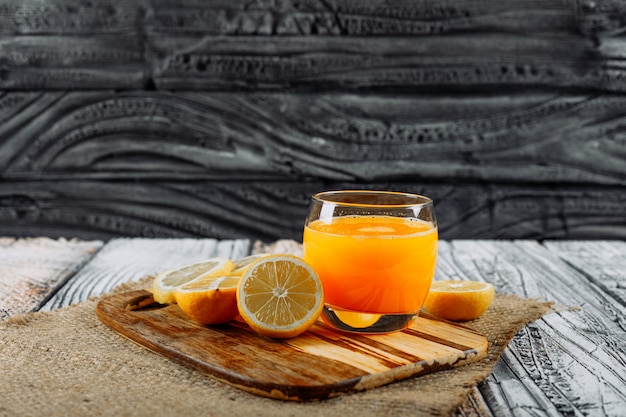 Limoni di vista laterale con le fette e il succo sul tagliere, sul panno e sul fondo di legno. spazio orizzontale per il testo