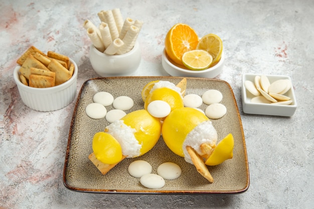 Limoni ghiacciati vista frontale con caramelle e biscotti sulla bevanda di frutta cocktail succo da tavola bianco