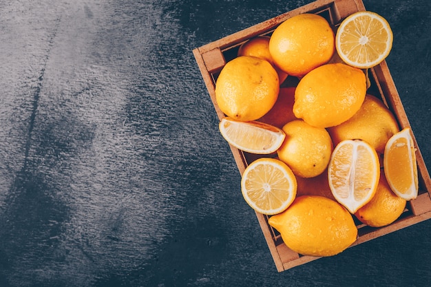 Limoni in una scatola di legno con vista dall'alto di fette su uno sfondo nero con texture spazio libero per il testo