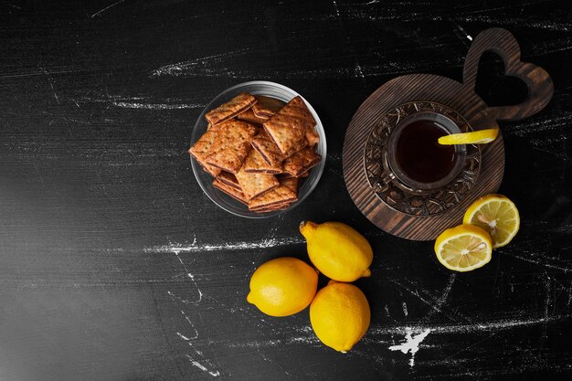 Limoni isolati su uno sfondo nero con un bicchiere di tè e cracker.