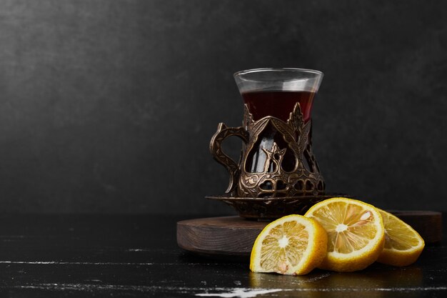 Limoni isolati su uno sfondo nero con un bicchiere di tè.