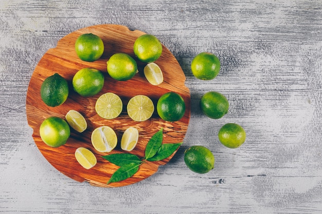 Limoni verdi di vista superiore in piattaforma di legno con le fette e le foglie su fondo di legno grigio. orizzontale