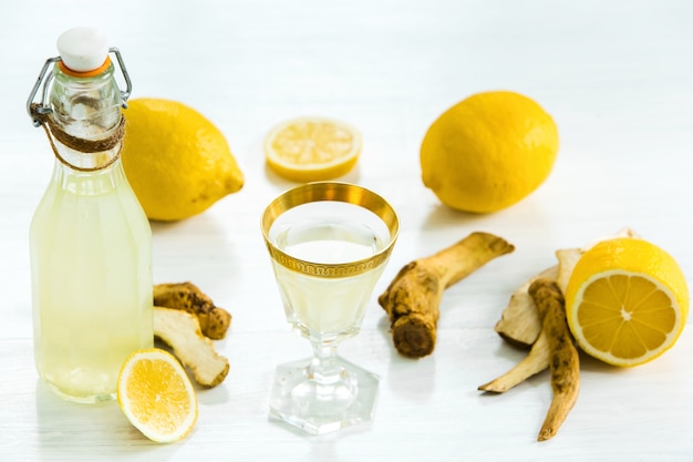 Liquore domestico della calce in un vetro e limoni e limette freschi su bianco