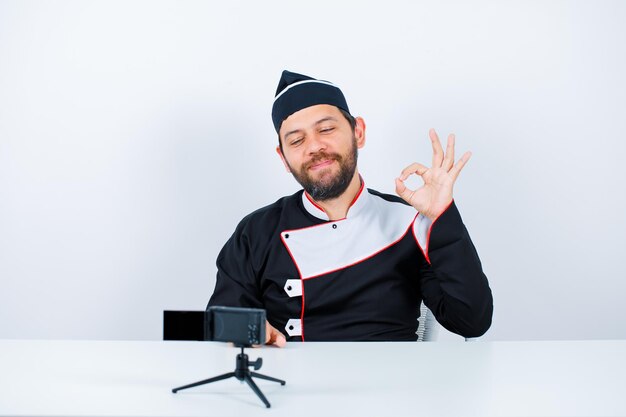 Lo chef del blogger sta girando bene il gesto sedendosi davanti alla sua mini telecamera su sfondo bianco