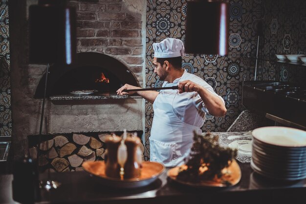 Lo chef esperto sta infornando la sua pizza usando una speciale spatola gigante.