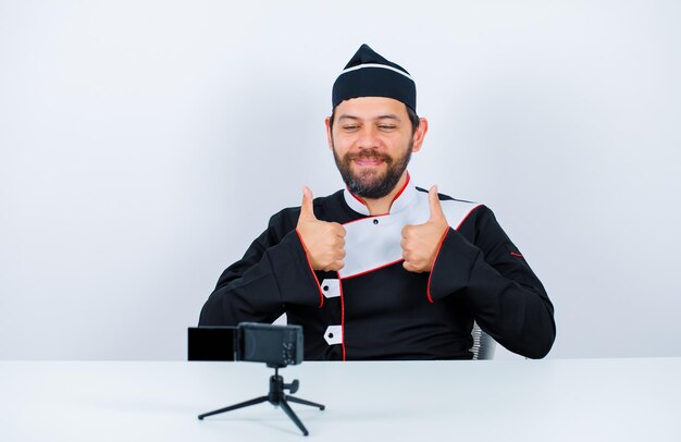 Lo chef sorridente del blogger sta posando davanti alla sua mini macchina fotografica mostrando gesti perfetti su sfondo bianco