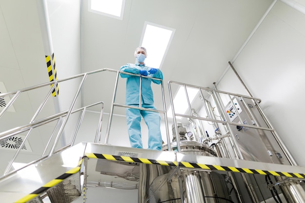 Lo scienziato è in piedi sulla scala, guarda la tuta da laboratorio blu della fotocamera con le mani incrociate dal muggito