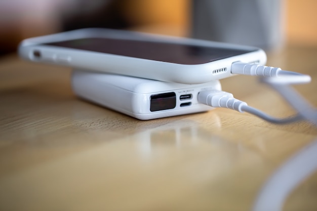 Lo smartphone viene caricato da un piccolo power bank bianco tramite un cavo, primo piano.