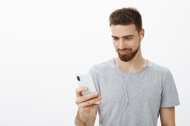 Lo sportivo che cerca la pista giusta inizia la pratica. Fiducioso, bello carismatico uomo barbuto con gli occhi azzurri che ascolta musica in auricolari che tiene smartphone sorridendo con gioia guardando lo schermo del cellulare