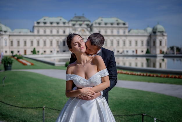 Lo sposo bacia il collo della sposa davanti all'enorme palazzo residenziale del re