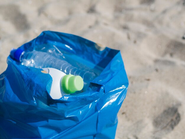 Lo spreco di plastica imbottiglia il sacchetto di immondizia blu sulla sabbia