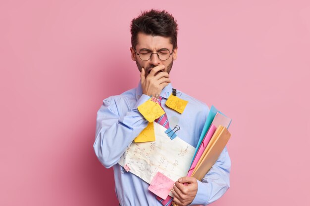 Lo studente stanco ha un'espressione assonnata copre la bocca con la mano e sbadiglia vestito con abiti formali si prepara per le pose degli esami