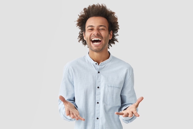 Lo studente uomo attraente gioioso e gioioso apre ampiamente la bocca, ride con gioia, esprime positività, vestito con una camicia elegante