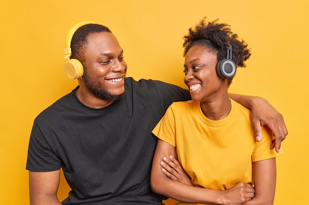 Lo studio dei migliori amici con la pelle scura ha un piacevole sorriso e mostra felicemente i denti bianchi ascolta la musica tramite cuffie wireless wireless