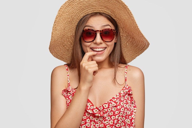 Foto gratuito lo studio ha sparato della donna attraente ha vacanze estive, sorride positivamente e tiene il dito vicino alla bocca