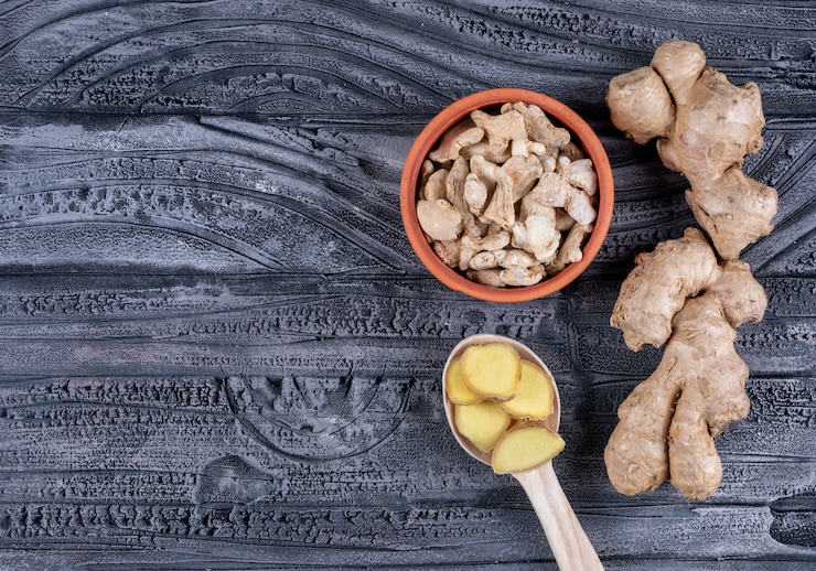 Foto gratuito lo zenzero in una ciotola e un cucchiaio di legno con le fette dello zenzero pianeggiano su un fondo di legno scuro, spazio per testo