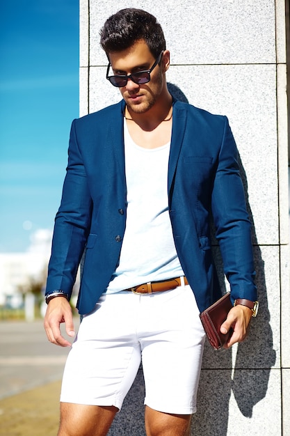 Look di alta moda. Giovane uomo di modello di uomo d'affari bello felice fiducioso alla moda in vestito blu copre la strada in occhiali da sole dietro il cielo