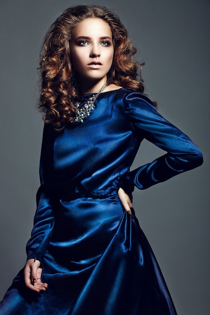 Look di alta moda. Ritratto glamour della bella bruna elegante caucasica giovane donna modello con trucco luminoso, con i capelli ricci sani in abito blu brillante