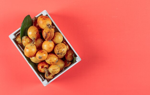 Loquat di vista superiore in scatola bianca con la foglia su fondo rosso-chiaro. spazio orizzontale per il testo