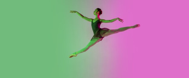 Luce. Giovane e graziosa ballerina isolata sul muro rosa-verde sfumato in neon. Arte, movimento, azione, flessibilità, concetto di ispirazione. Ballerina flessibile, salti senza peso.