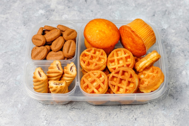 Lunch box malsano con biscotti, waffles.muffins sulla superficie del calcestruzzo