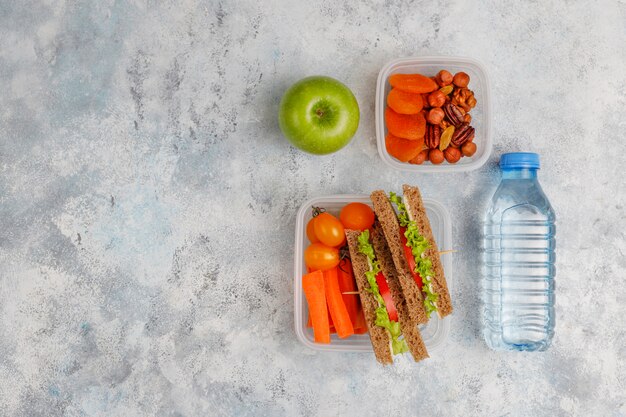 Lunchbox con sandwich, verdure, frutta su bianco.