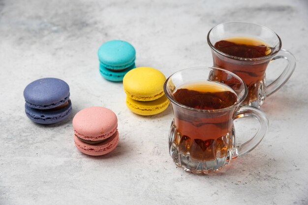 Macarons colorati con due tazze di tè nero su superficie bianca.