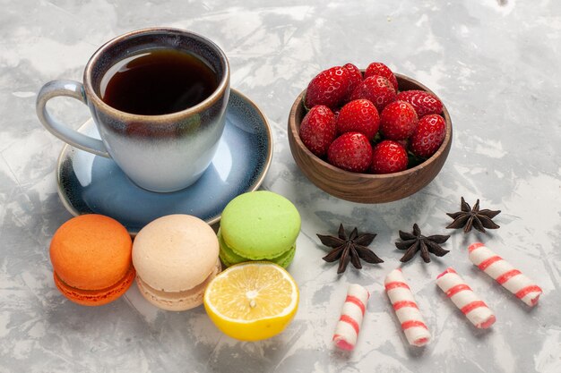 Macarons francesi di vista frontale con la tazza di tè sul biscotto dolce della torta di zucchero del biscotto della torta bianca della scrivania