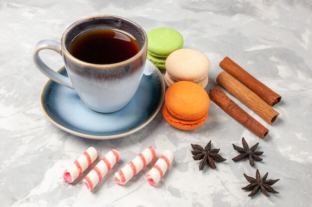 Macarons francesi di vista frontale con la tazza di tè sul biscotto dolce della torta di zucchero della torta di superficie bianca