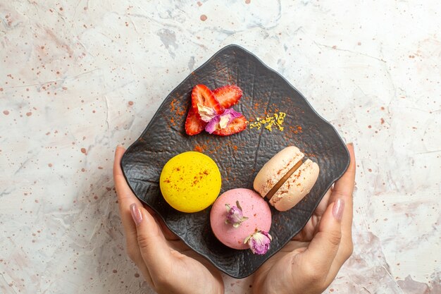 Macarons francesi di vista superiore all'interno del piatto sulla torta dolce del biscotto del biscotto della tavola bianca