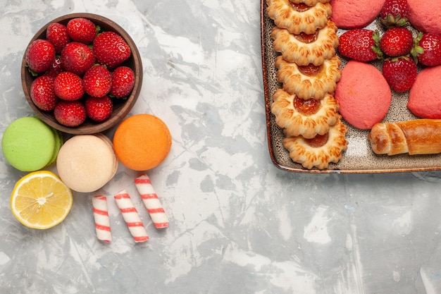 Macarons francesi di vista superiore con fragole rosse fresche sulla superficie bianca