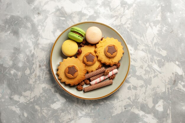 Macarons francesi di vista superiore con torte e biscotti sulla torta dolce della torta dello zucchero del biscotto dei biscotti di superficie bianca