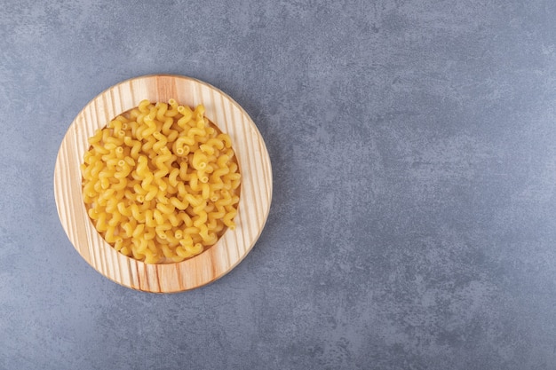 Maccheroni asciutti crudi sul piatto di legno.