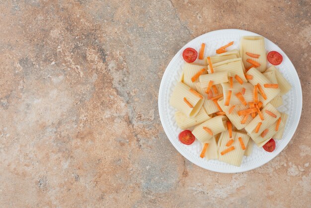 Maccheroni con carote e pomodorini sul piatto bianco.