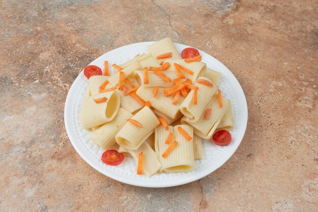 Maccheroni con carote e pomodorini sul piatto bianco.