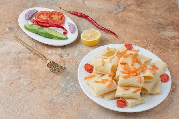 Maccheroni con carote, pomodorini, cetrioli e fetta di limone sul piatto bianco