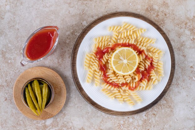 Maccheroni con porzioni di ketchup e peperoni sott'aceto su superficie di marmo.