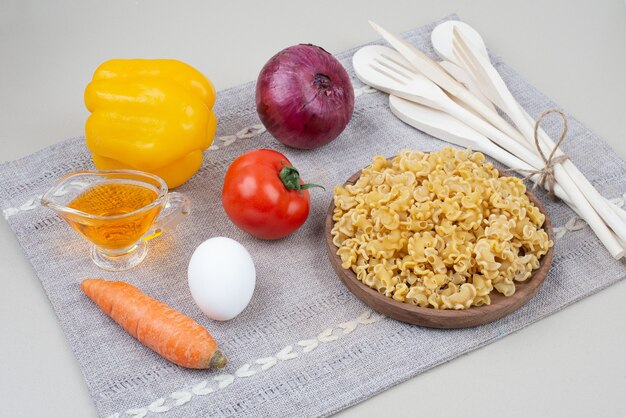 Maccheroni crudi con le verdure sul piatto di legno sulla tovaglia