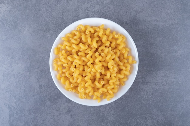 Maccheroni crudi del gomito sul piatto bianco.